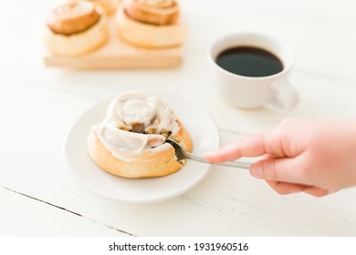 Woman Using A Fork To Eat A Tasty Cinnamon Roll With A Cup Of Coffee On Her Kitchen Table. Caucasian Woman Eating And Enjoying A Sweet Snack 