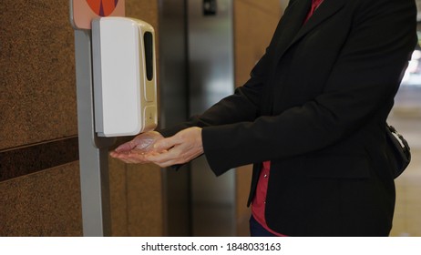 woman using a hand sanitizer station in an office building during covid.