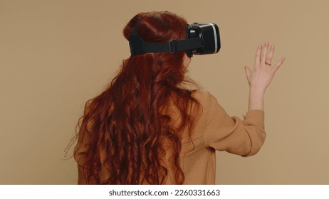 Woman using headset helmet to play simulation game app online. Watching virtual reality 3D 360 video content. Girl in VR goggles isolated on studio beige background. Futuristic technology. Rear view - Powered by Shutterstock