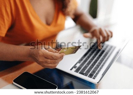 Woman using her gold credit card to make an online payment with a laptop, enjoying the rewards of being a loyal customer. Black female retiree making smart banking choices and maximizing her benefits.