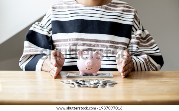 A woman\
is using her hand to protect the piggy bank and money on the desk,\
she is organizing money to divide it into savings and buy funds to\
make it grow. Personal finance\
concept.