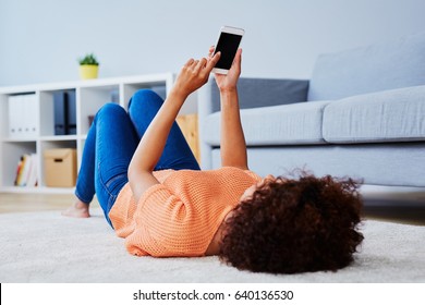 Woman using her phone lying on carpet in living room
