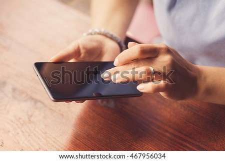 A woman is using her smart phone at a table outside