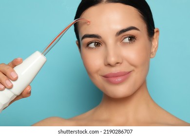 Woman using high frequency darsonval device on light blue background - Shutterstock ID 2190286707