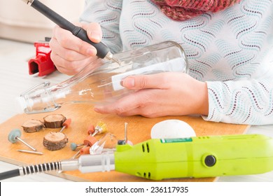 Woman using a high speed rotary multi tool to engrave ornament on the bottle