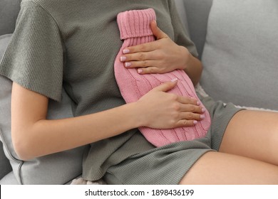 Woman Using Hot Water Bottle To Relieve Menstrual Pain On Sofa At Home, Closeup