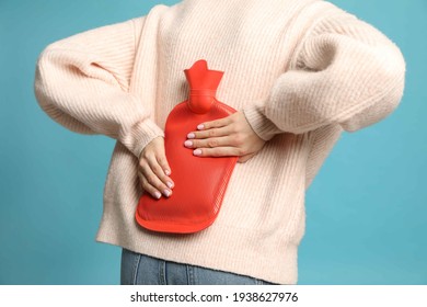 Woman Using Hot Water Bottle To Relieve Back Pain On Light Blue Background, Closeup