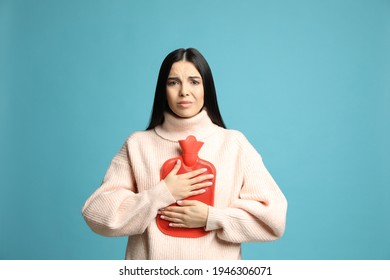 Woman Using Hot Water Bottle To Relieve Chest Pain On Light Blue Background