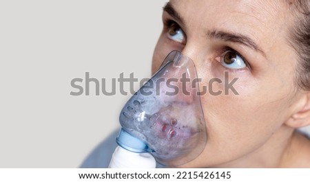 woman using inhaler nebulizer for respiratory diseases treatment concept,physiological solution salted water.girl looks up isolated light background.inhalation at home free space copy paste mock up
