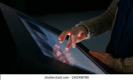 Woman using interactive touchscreen display in modern historical museum. Evening time, lowlight. Education and entertainment concept. Close up shot