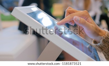 Woman using interactive touchscreen display at urban exhibition - scrolling and touching. Entertainment and technology concept