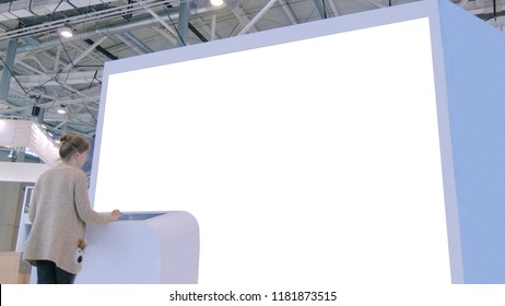 Woman Using Interactive Touchscreen Terminal In Front Of White Empty Large Display At Urban Exhibition. Mock Up And Technology Concept