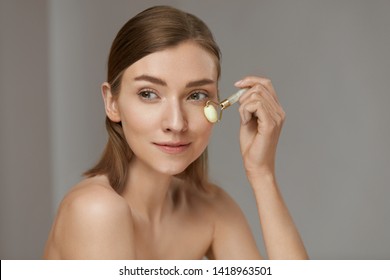 Woman Using Jade Facial Roller For Face Massage At Home. Girl Using Natural Massager Tool For Skin Care And Spa Beauty Treatment Closeup Portrait