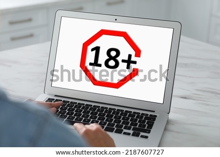 Woman using laptop with age limit sign 18+ years indoors, closeup