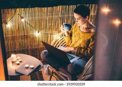  Woman using laptop at balcony of her apartment at the night.