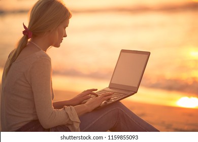 Woman using a laptop at the beach during sunset.  - Powered by Shutterstock