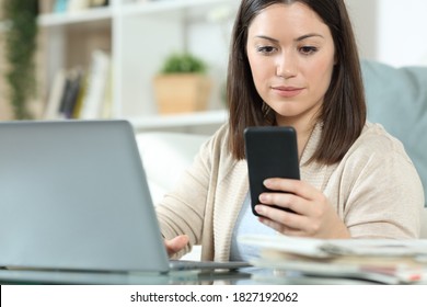 Woman using a laptop and checking a smart phone sitting in the living room at home