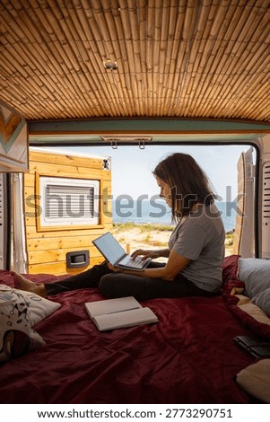 Woman using laptop computer inside van on a bed with ocean view, embodying remote work