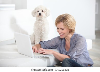 Woman Using Laptop Computer Next To Small White Dog