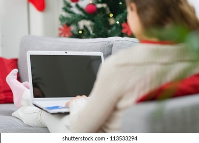 Woman Using Laptop Near Christmas Tree. Rear View