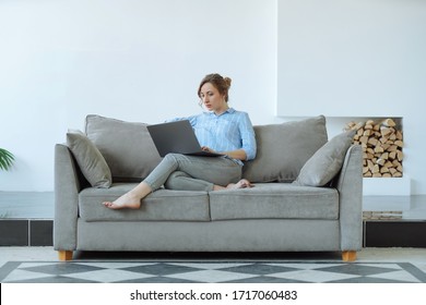 Woman using laptop on a couch alone at home during quarantine. Big bright living room