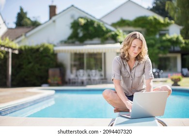 Woman Using Laptop On Diving Board At Poolside