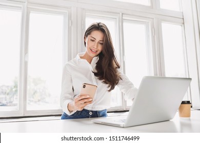 Woman using laptop and smartphone in office. Beautiful girl looking at mobile phone. Entrepreneur, businesswoman, freelance worker, student working on computer at home. Business, technology concept