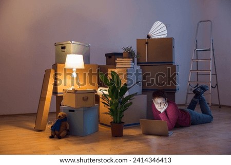 Woman using laptop surrounded by cardboard boxes in a new home
