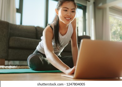 Woman Using Laptop While Exercising At Home. Female In Sportswear Sitting On Floor And Watching Exercise Video For Her Workout.