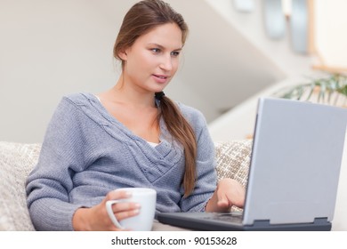 Woman using a laptop while having a coffee in her living room. Working from home in quarantine lockdown. Social distancing Self Isolation