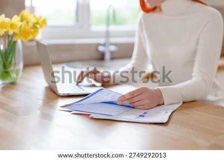 Woman using laptop while sorting papers in a kitchen during daytime