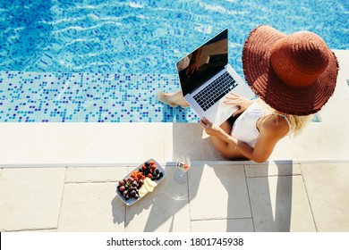 woman using laptop working remotely near swimming pool and travel. Sexy woman browsing and typing on laptop on self isolation quarantine at home pool outdoors with dog.