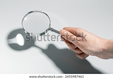 Woman using magnifying glass, searching, analyzing documents. Business research, detective work in office setting. Focused investigation, quality check through magnifying tool.