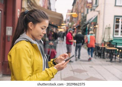 Woman using mobile phone app while walking in city street to find a store direction on map or order online at restaurant. Asian woman canadian city lifestyle.