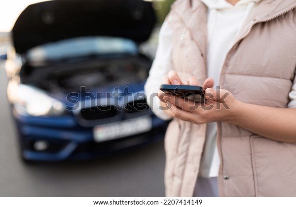 a woman using a mobile phone calls an emergency\
service to evacuate a car next to a car with an open hood, traffic\
accident concept