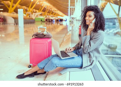 woman using mobile phone and laptop at the airport sitting at the window