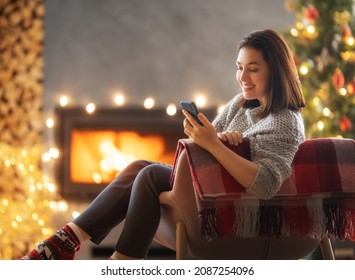 Woman is using mobile phone sitting near Christmas tree. - Powered by Shutterstock