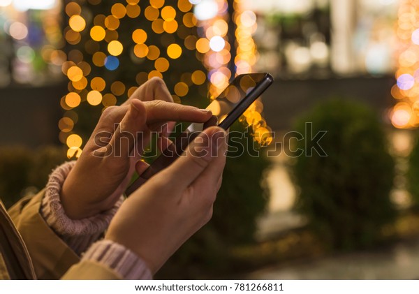 Woman using\
Mobile Phone in the street before christmas , urban life night\
light and color bokeh Background. Female using her mobile phone,\
city skyline night light\
background