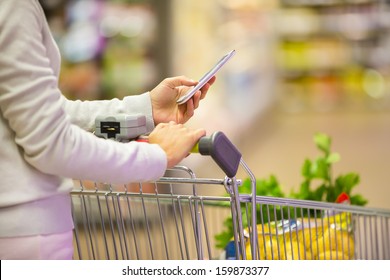 Woman Using Mobile Phone While Shopping In Supermarket, Trolley 
