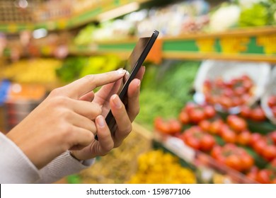Woman Using Mobile Phone While Shopping In Supermarket, Vegetable Department Store