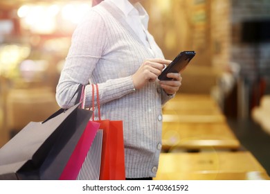 Woman Using Mobile Phone While Holding Shopping Bags