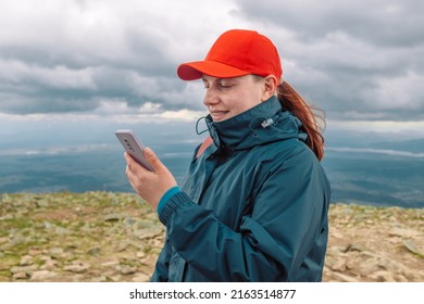 Woman Using Mobile Phone While Hiking Up A Mountain. Female Mountaineer Looking At Her Phone While Climbing A Peak. 