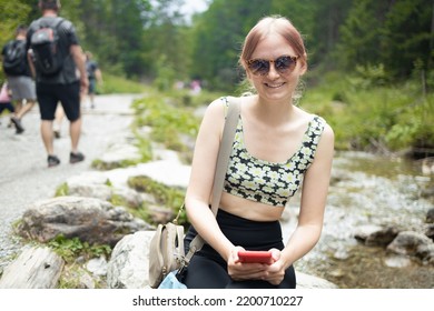 Woman Using Mobile Phone While Hiking Up A Mountain. Female Mountaineer Looking At Her Phone While Climbing A Peak. 