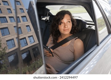 Woman using mobile while sitting in the car. Pregnant female living daily life. Maternity and mobility. Shoot from the open windows. Cell phone and connectivity