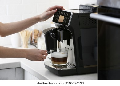 Woman using modern espresso machine for making coffee with milk in kitchen, closeup