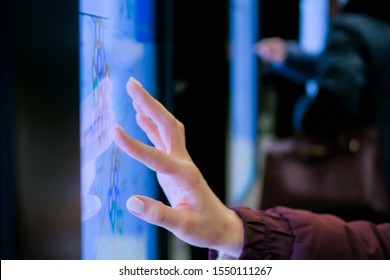 Woman using modern interactive touchscreen display of electronic multimedia kiosk with city map at street - scrolling and touching - evening time. Navigation, journey and technology concept