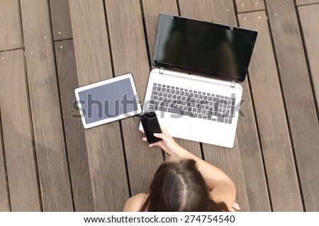 Woman using multiple devices phone laptop and tablet lying in a wood bench in a park