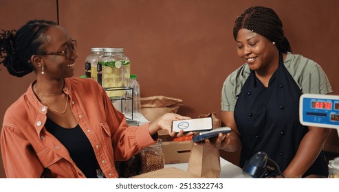 Woman using nfc mobile payment to purchase organic food, visiting local seller to restock pantry supplies. Vegan client paying with smartphone at checkout, eco friendly concept. Handheld shot. - Powered by Shutterstock