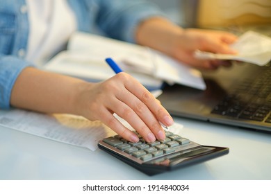 woman using a pen writing on bank account book while holding the bills to calculate in living room at home. Expenses, account, taxes, home budget concept.