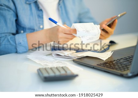 woman using a pen writing on bank account book while holding the bills to calculate in living room at home. Expenses, account, taxes, home budget concept